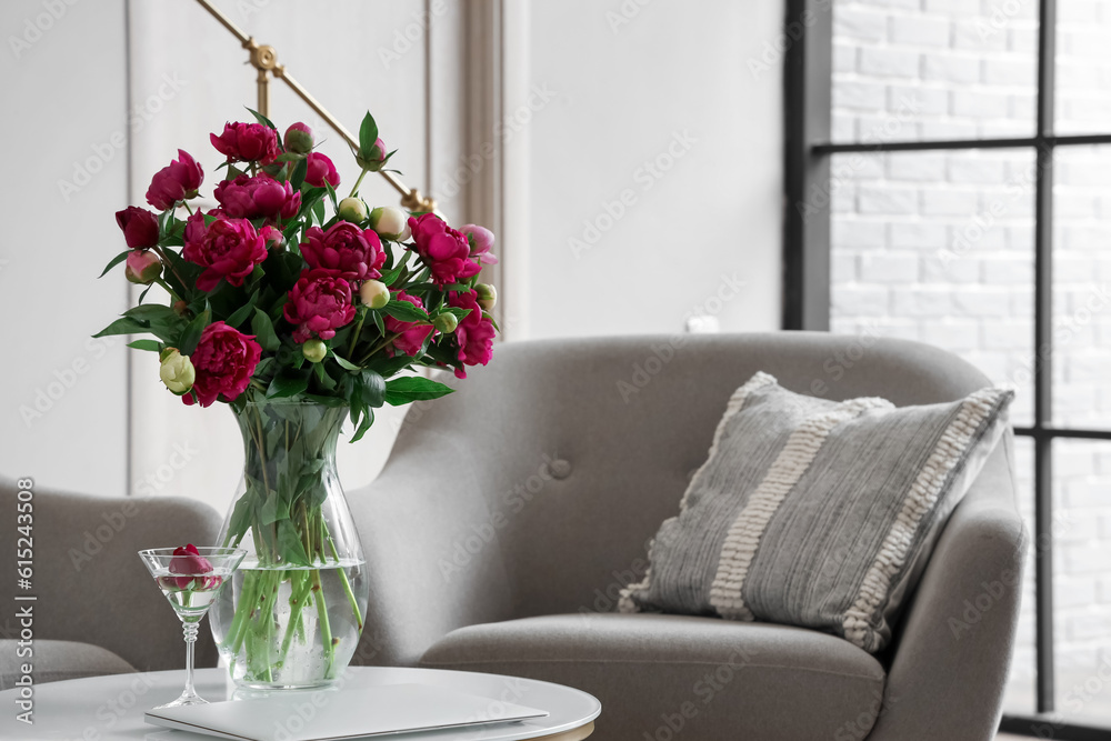 Vase with red peonies, glass and laptop on coffee table in living room