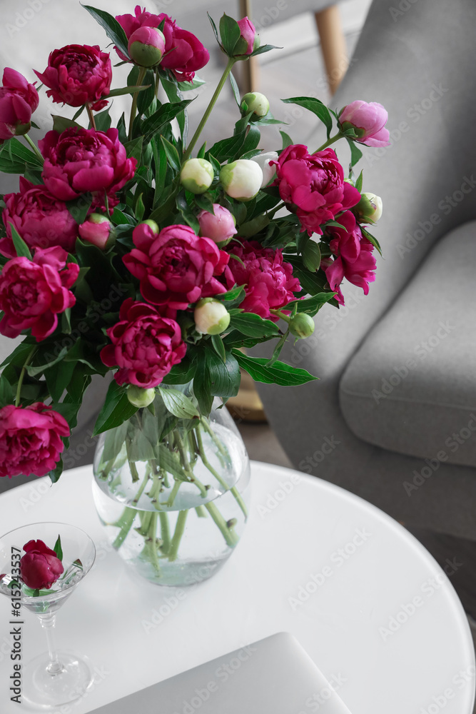 Vase with red peonies, glass and laptop on coffee table in living room