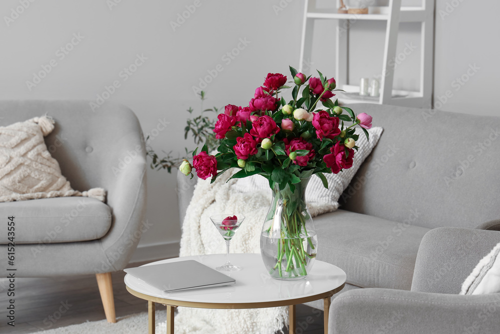 Vase with red peonies, glass and laptop on coffee table in living room