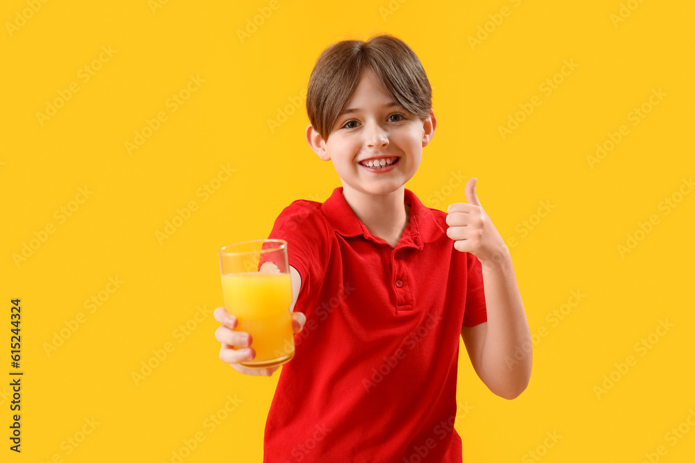 Little boy with glass of orange juice showing thumb-up on yellow background