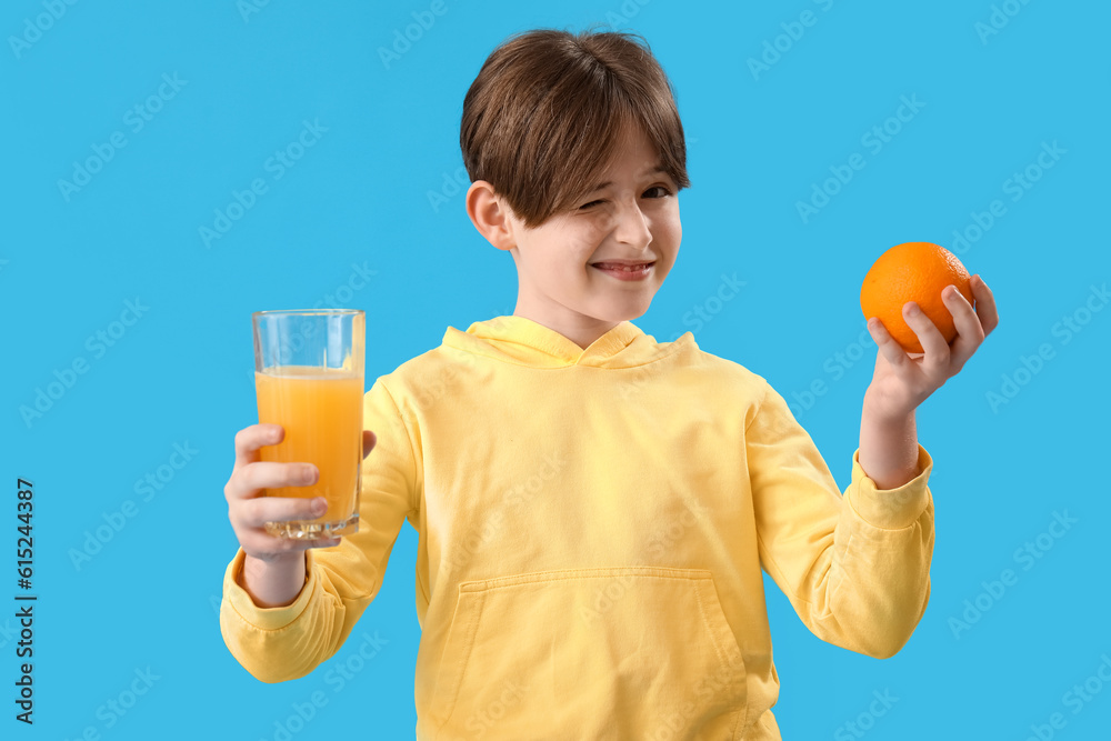 Little boy with orange and glass of juice on blue background