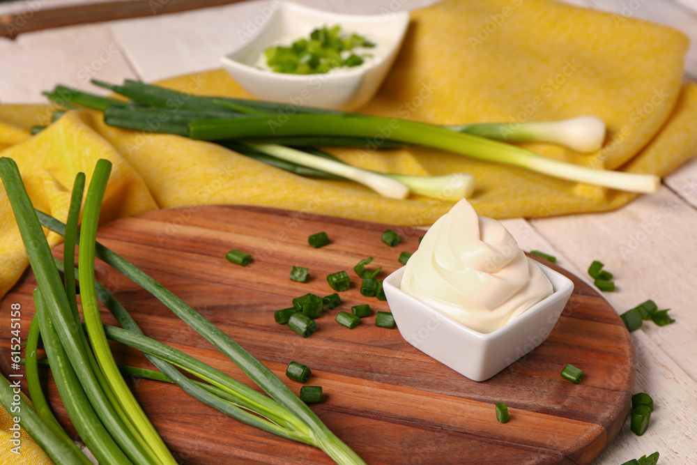 Bowls of tasty sour cream and sliced green onion on white wooden background