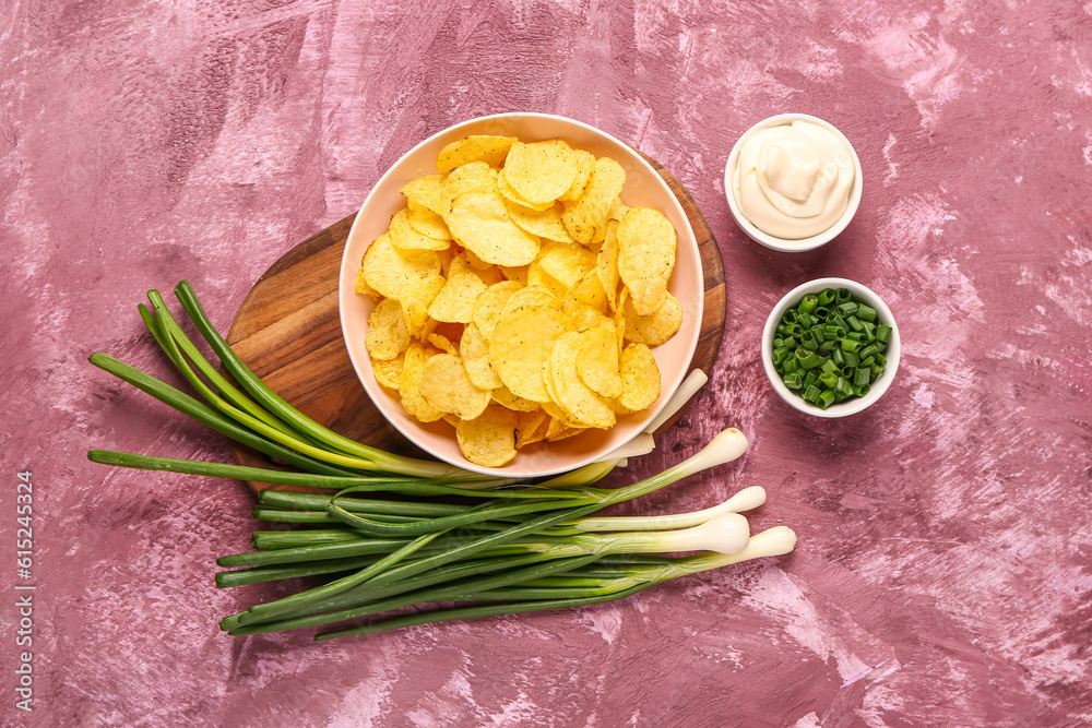 Bowls of tasty sour cream with sliced green onion and potato chips on purple background