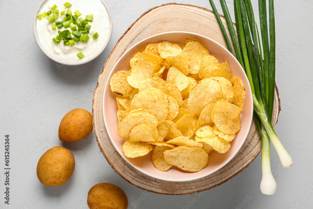 Bowl of tasty sour cream with sliced green onion and potato chips on grey background