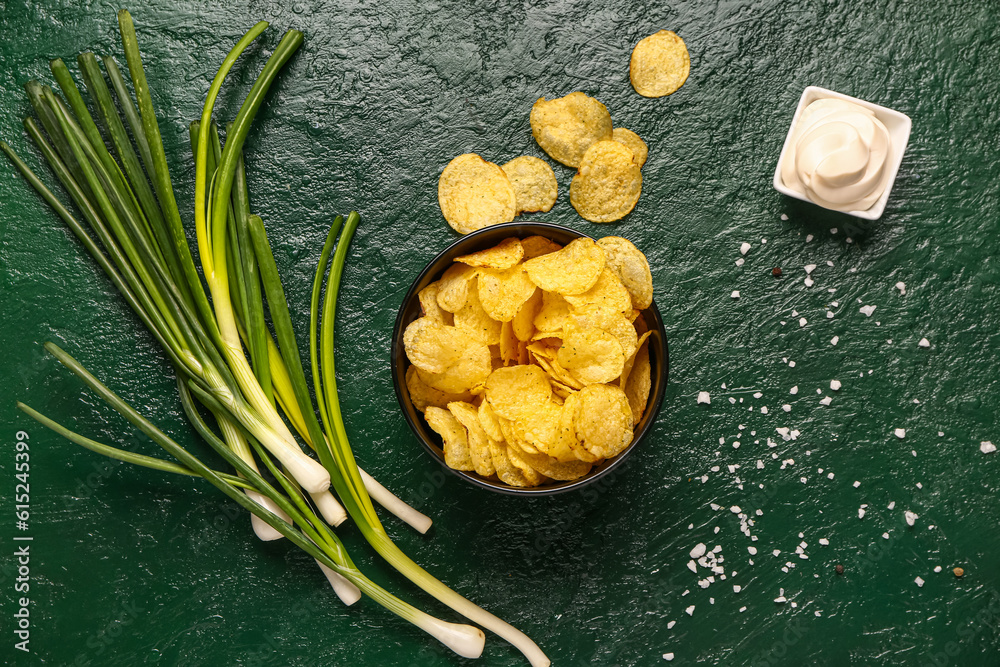 Bowl of tasty sour cream with scallion and potato chips on green background