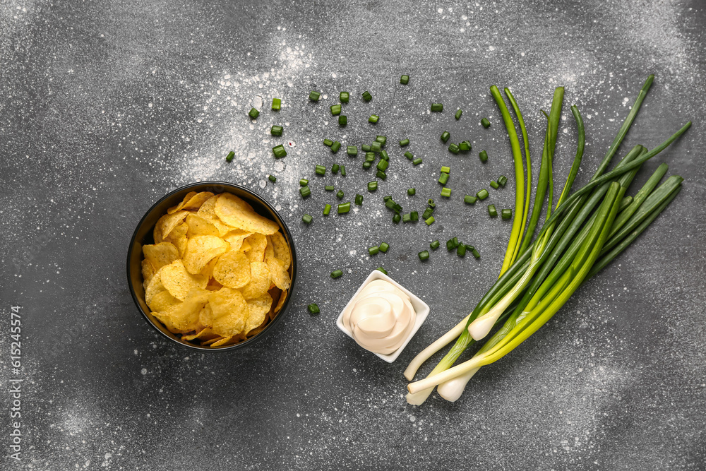 Bowl of tasty sour cream with sliced green onion and potato chips on grey background