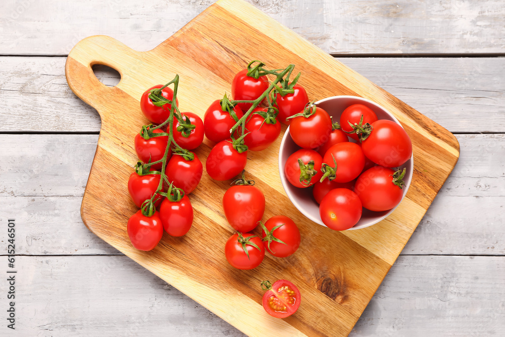 Board and bowl with fresh cherry tomatoes on grey wooden background