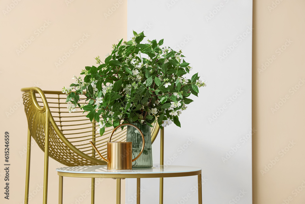 Vase with blooming jasmine flowers on coffee table and stylish armchair near beige wall