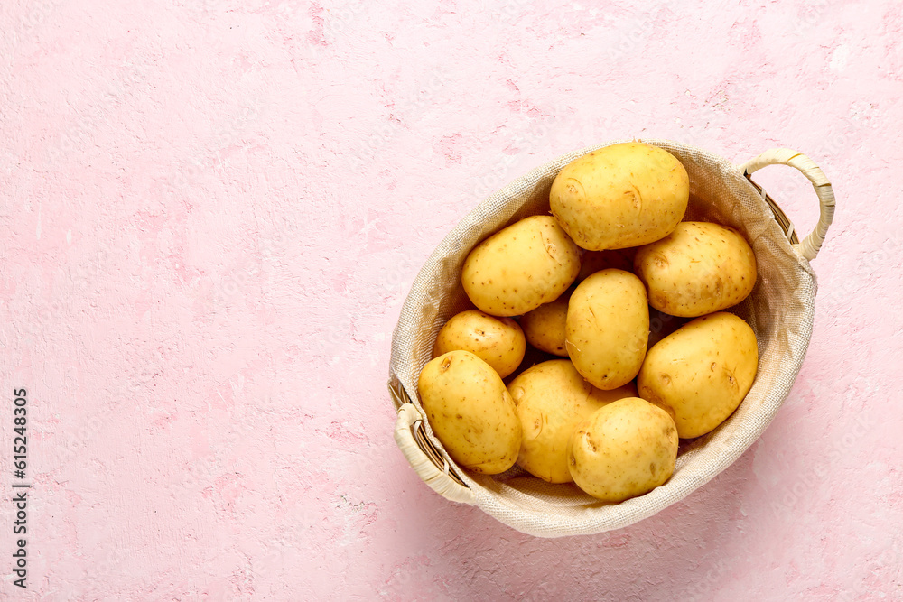 Wicker basket with raw baby potatoes on pink background