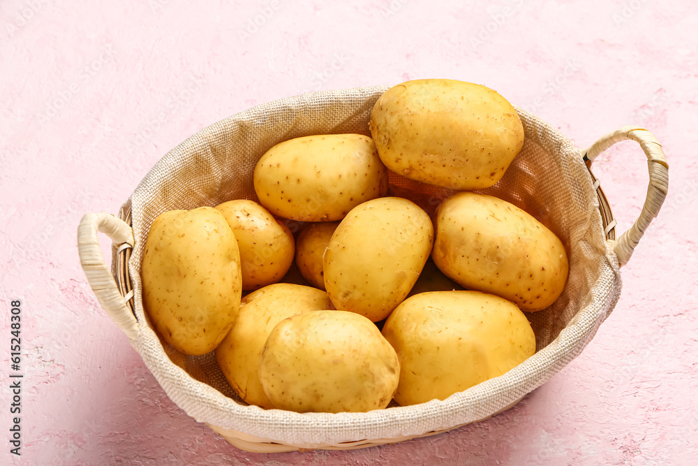 Wicker basket with raw baby potatoes on pink background