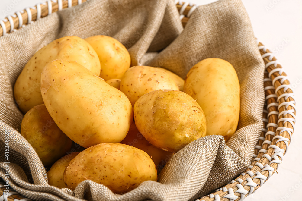 Wicker bowl with raw baby potatoes on white background, closeup