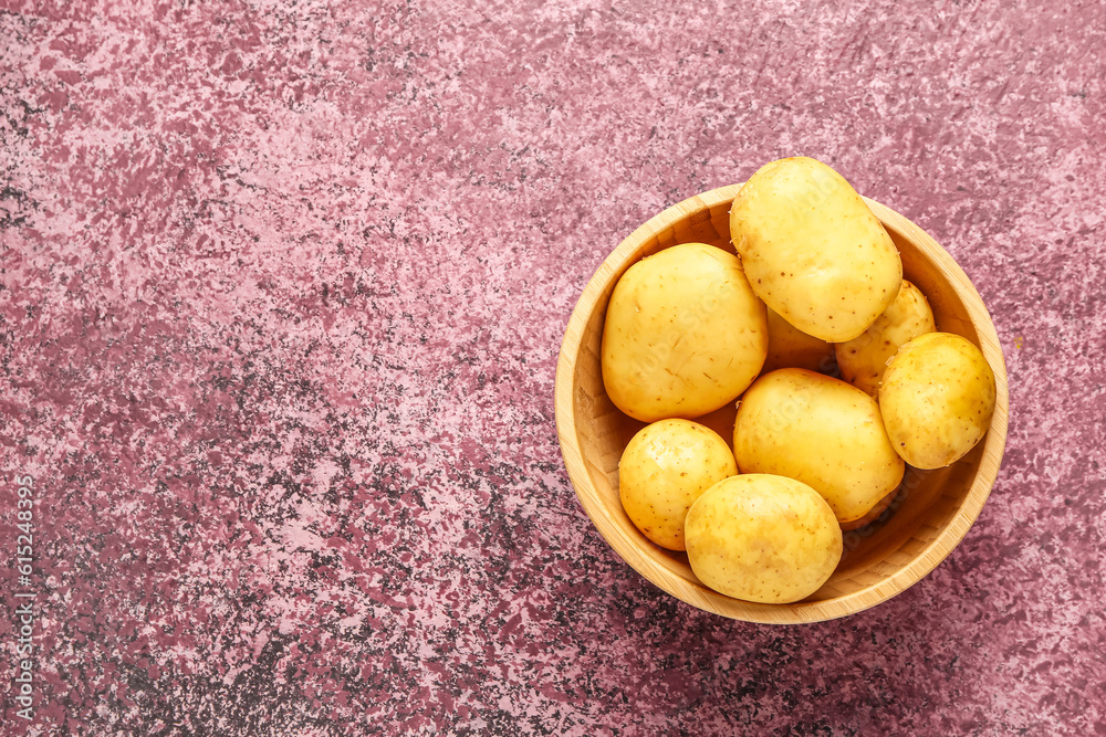 Wooden bowl with raw baby potatoes on purple background