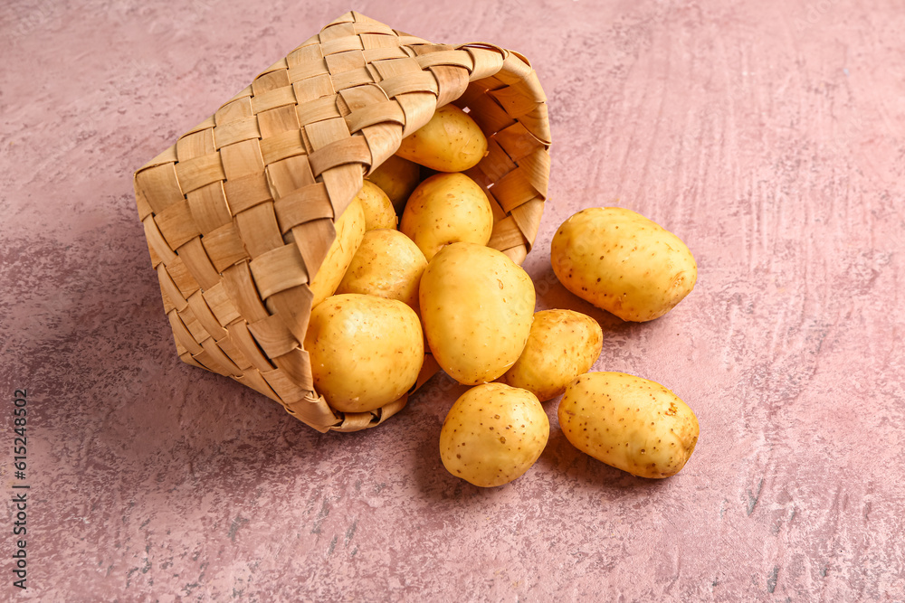 Wicker basket with raw baby potatoes on pink background