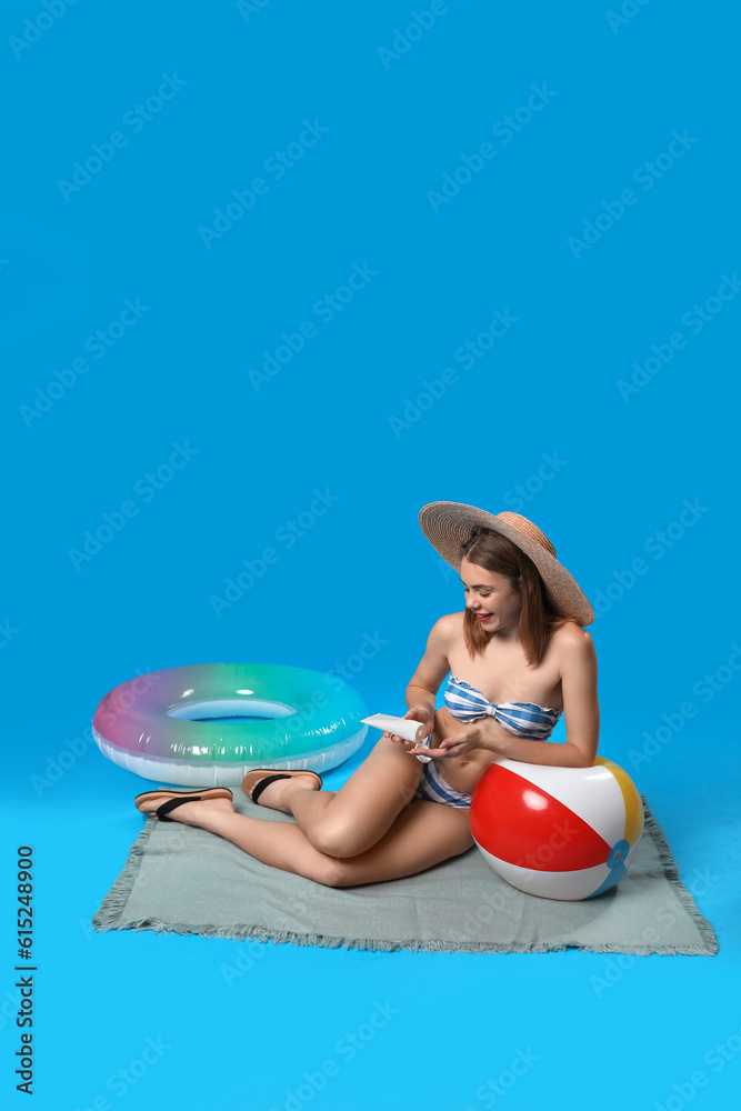 Young woman in swimsuit applying sunscreen on blue background