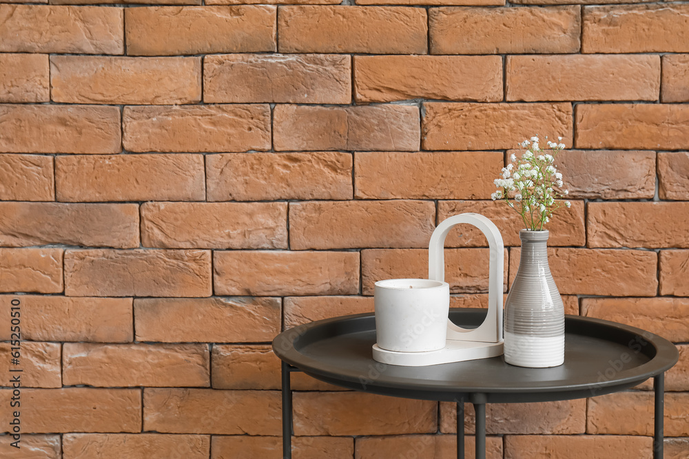 Gypsophila flowers and candle on table near brick wall in room