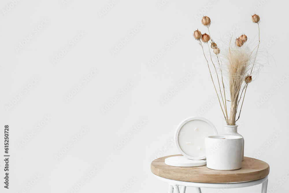 Dried flowers and candles on table near light wall in room