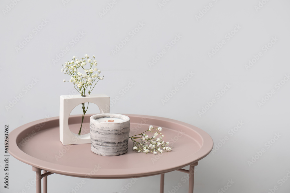 Gypsophila flowers and candle on table near light wall in room