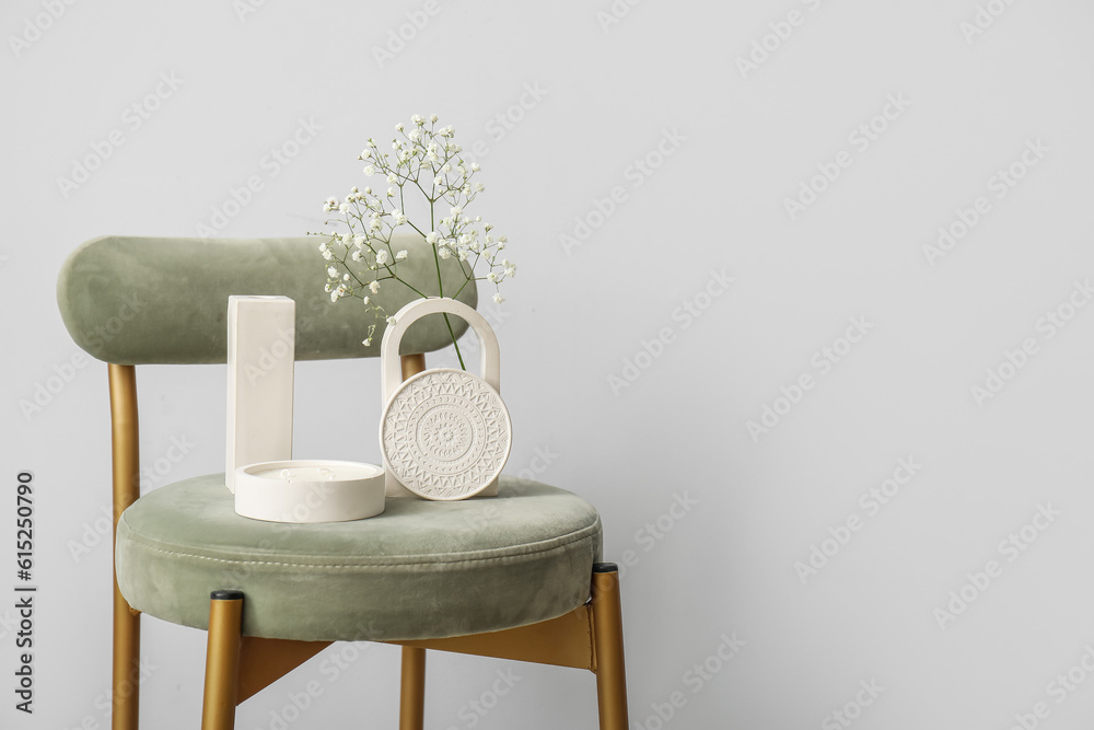 Gypsophila flowers and candle on chair near light wall in room