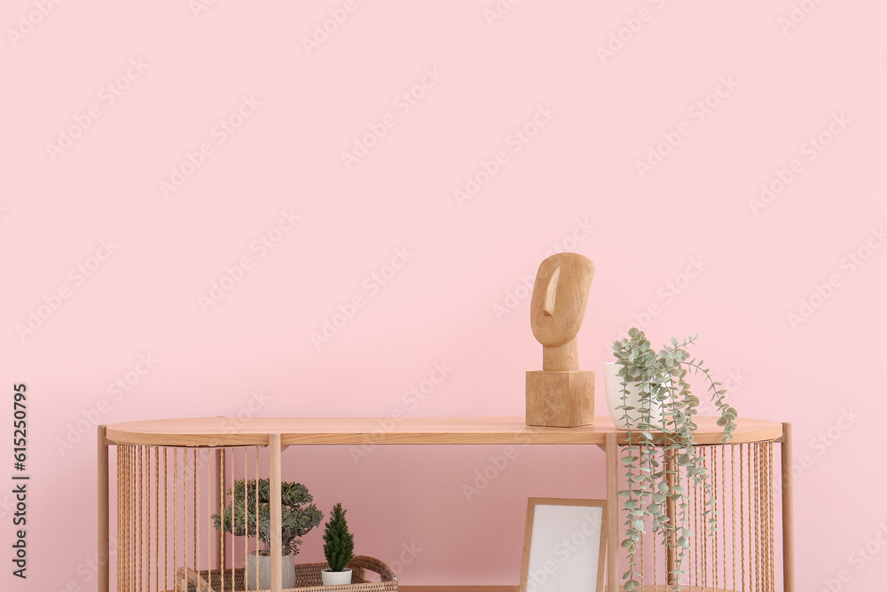 Modern shelving unit with houseplants and decor near pink wall in room