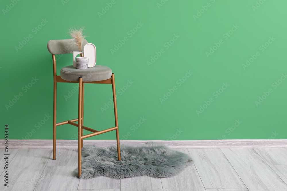 Holder with candle, pampas grass on chair and rug near green wall in room