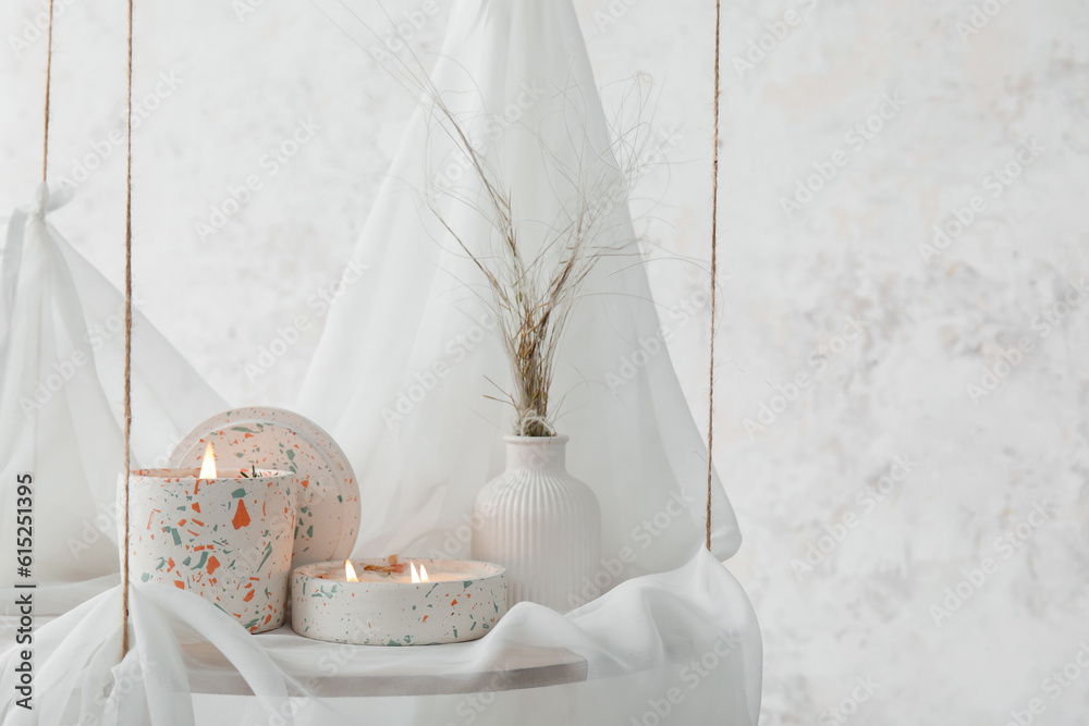 Holders with burning candles on hanging shelf near light wall in room, closeup