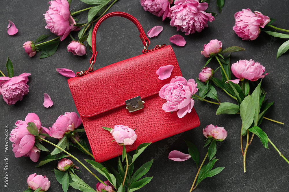 Composition with stylish female bag and beautiful peony flowers on dark background