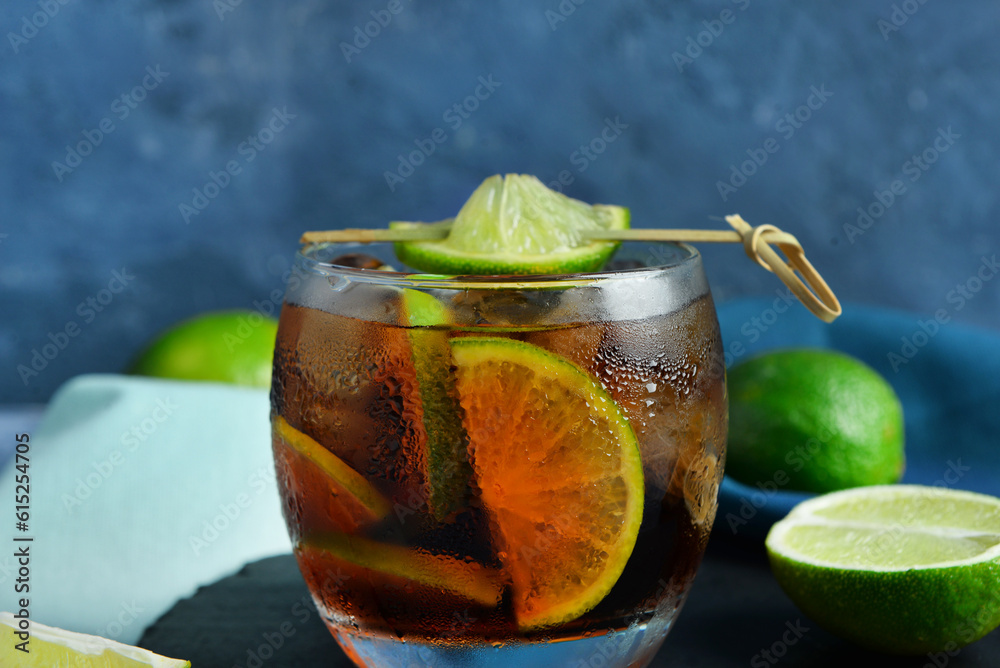 Board with glass of cold Cuba Libre cocktail and limes, closeup