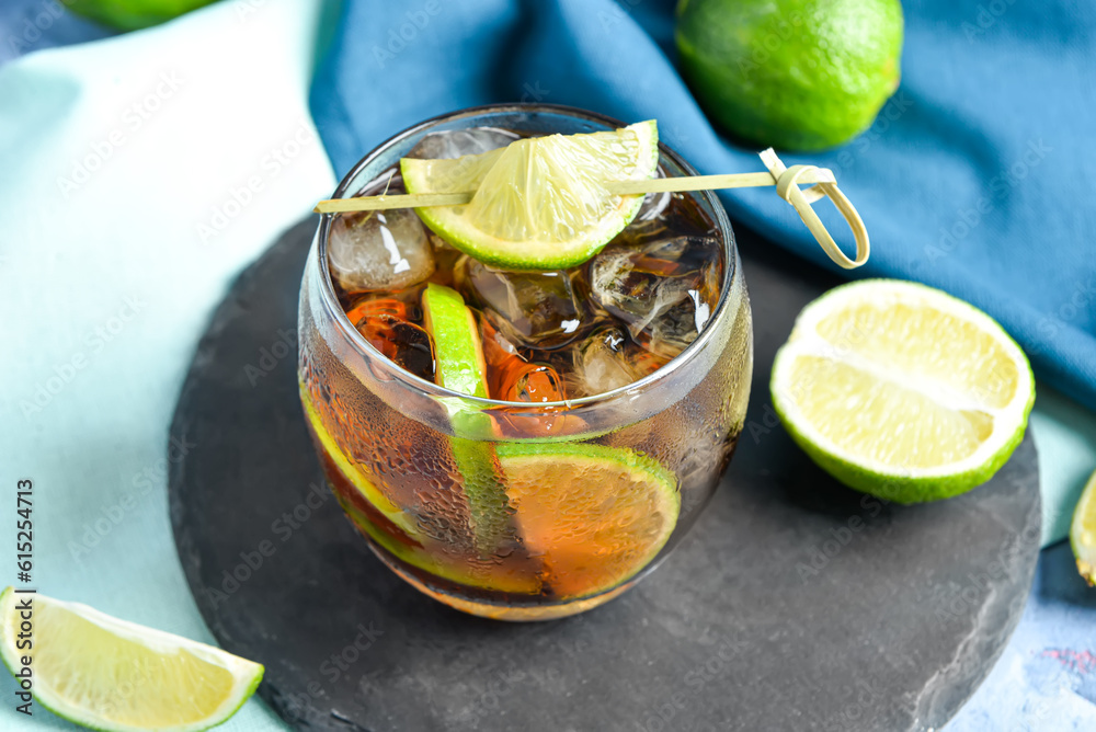 Board with glass of cold Cuba Libre cocktail and limes, closeup