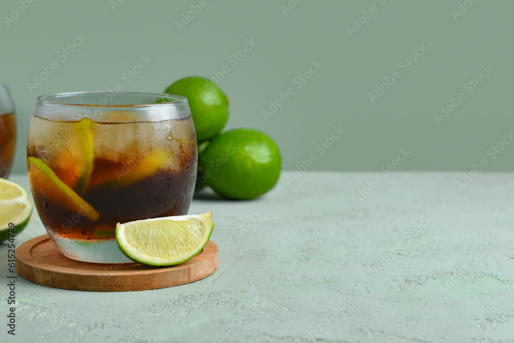 Glass of cold Cuba Libre cocktail and limes on grey background