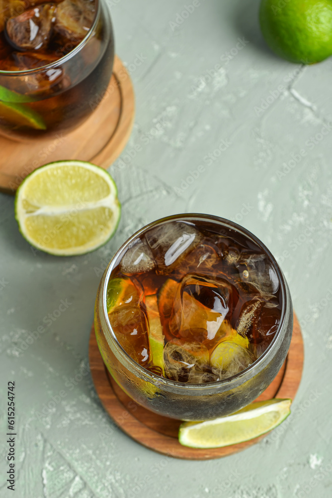 Glasses of cold Cuba Libre cocktail and limes on grey background