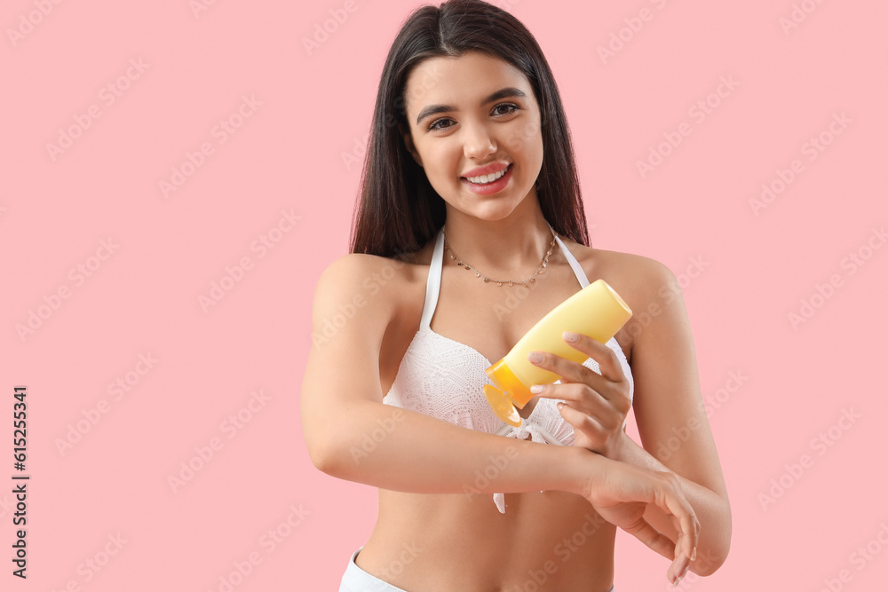 Young woman applying sunscreen cream on pink background