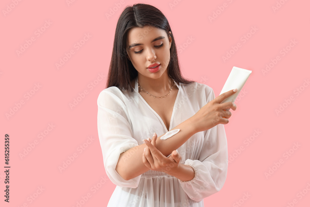 Young woman applying sunscreen cream on pink background