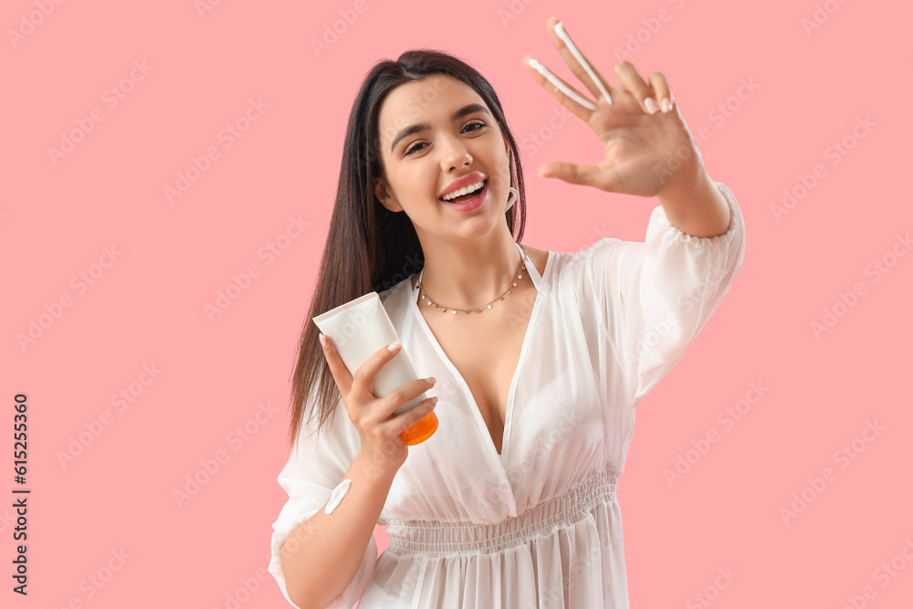 Young woman with sunscreen cream on pink background