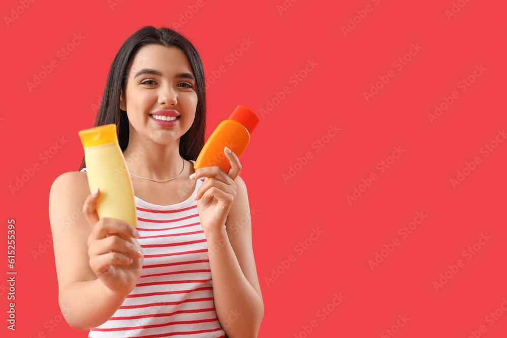 Young woman with bottles of sunscreen cream on red background