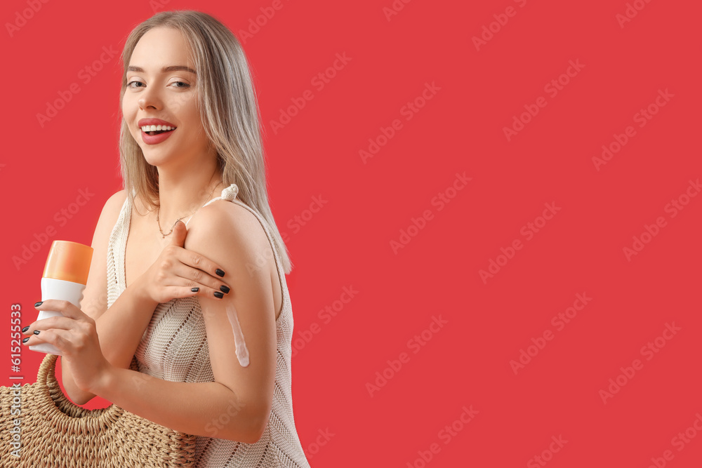 Young woman applying sunscreen cream on red background