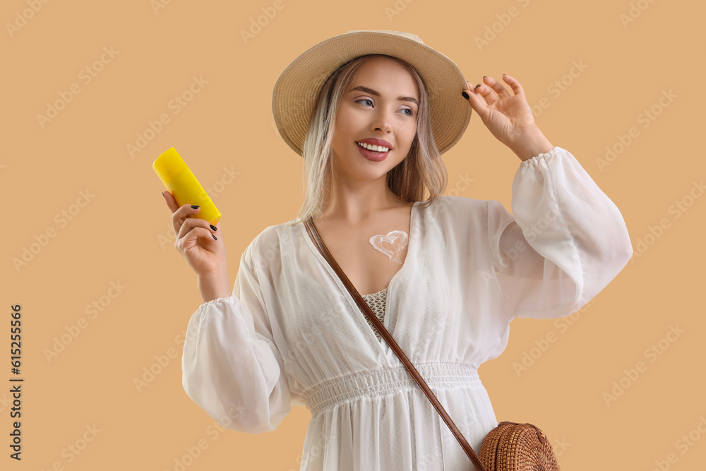 Young woman with sunscreen cream on beige background