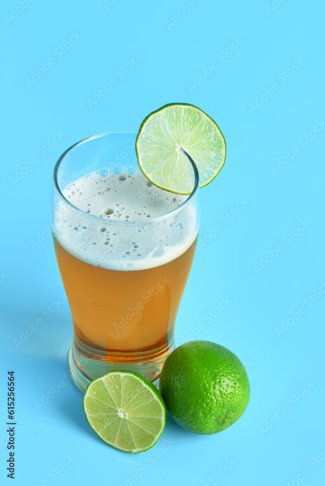 Glass of cold beer with lime on blue background