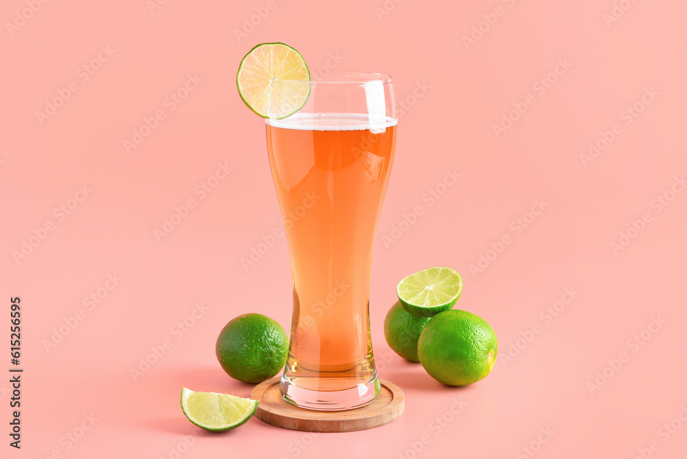 Glass of cold beer with lime on pink background