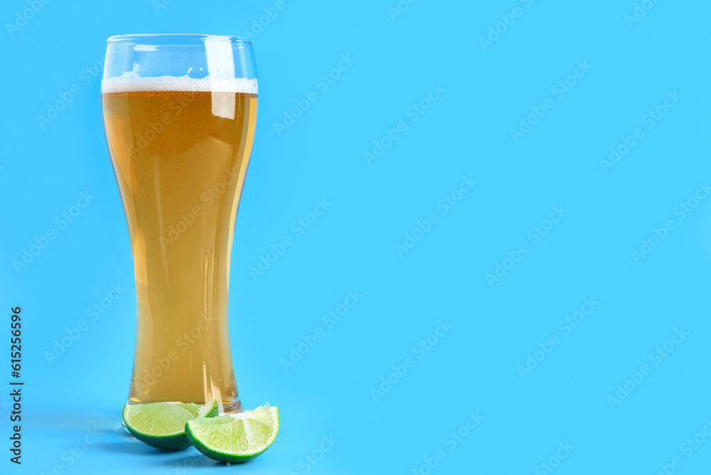 Glass of cold beer with lime on blue background