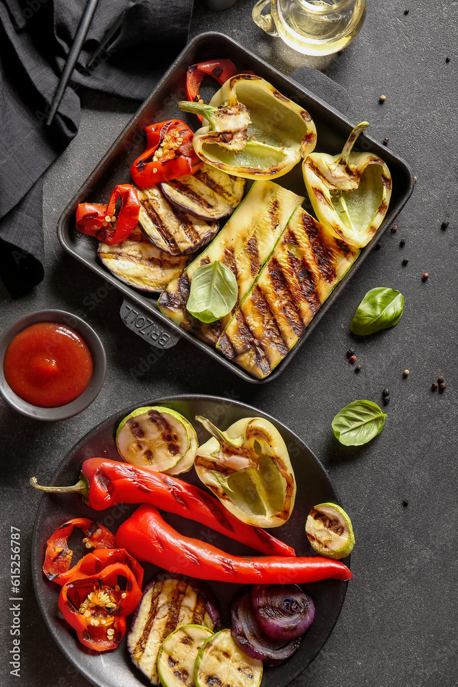 Plate and baking dish with tasty grilled vegetables on black background