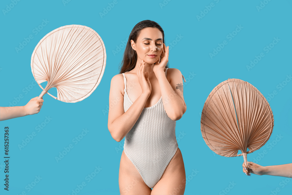 Young woman with sunscreen cream and fans on blue background