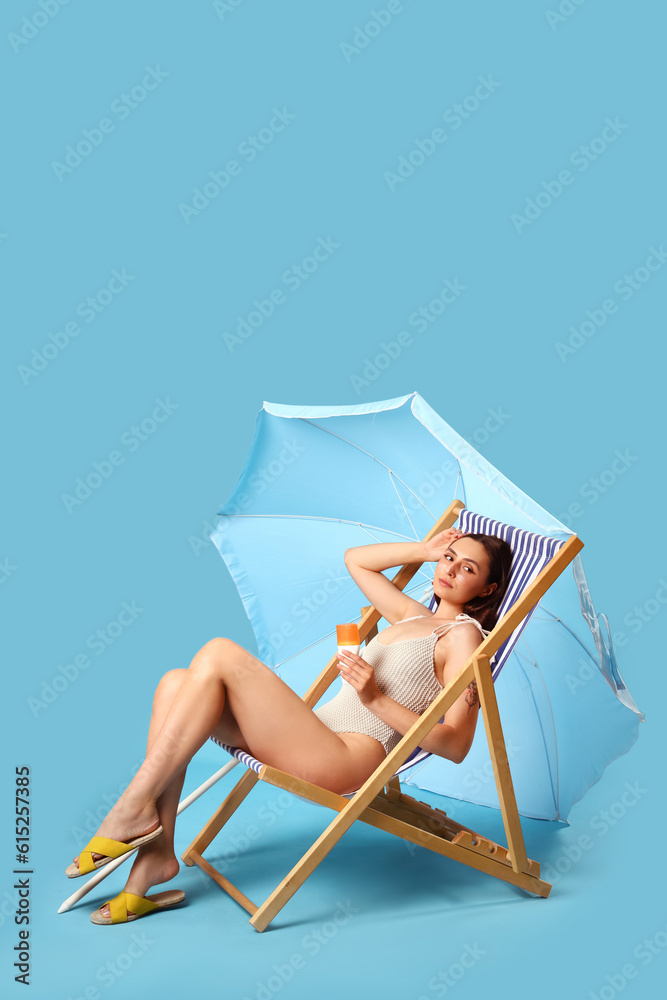 Young woman with sunscreen cream in deck chair on blue background