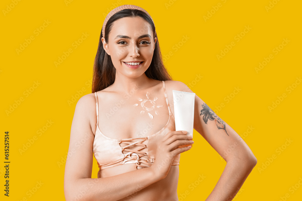 Young woman with sunscreen cream on yellow background