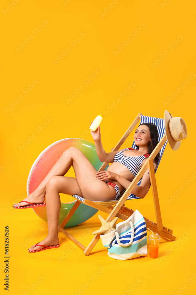 Young woman with sunscreen cream in deck chair on yellow background