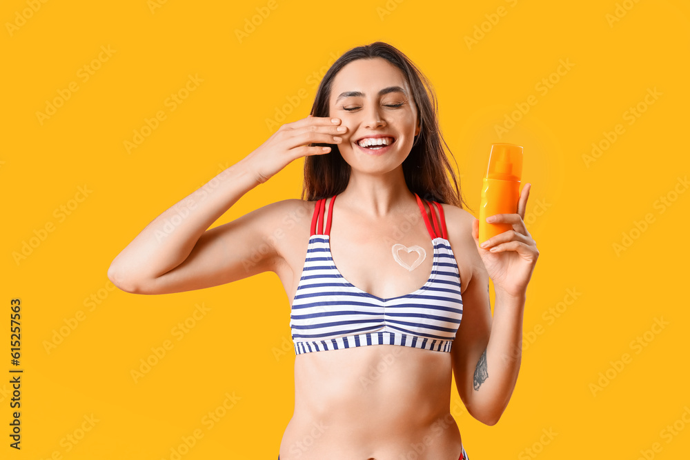 Young woman with heart made of sunscreen cream on orange background