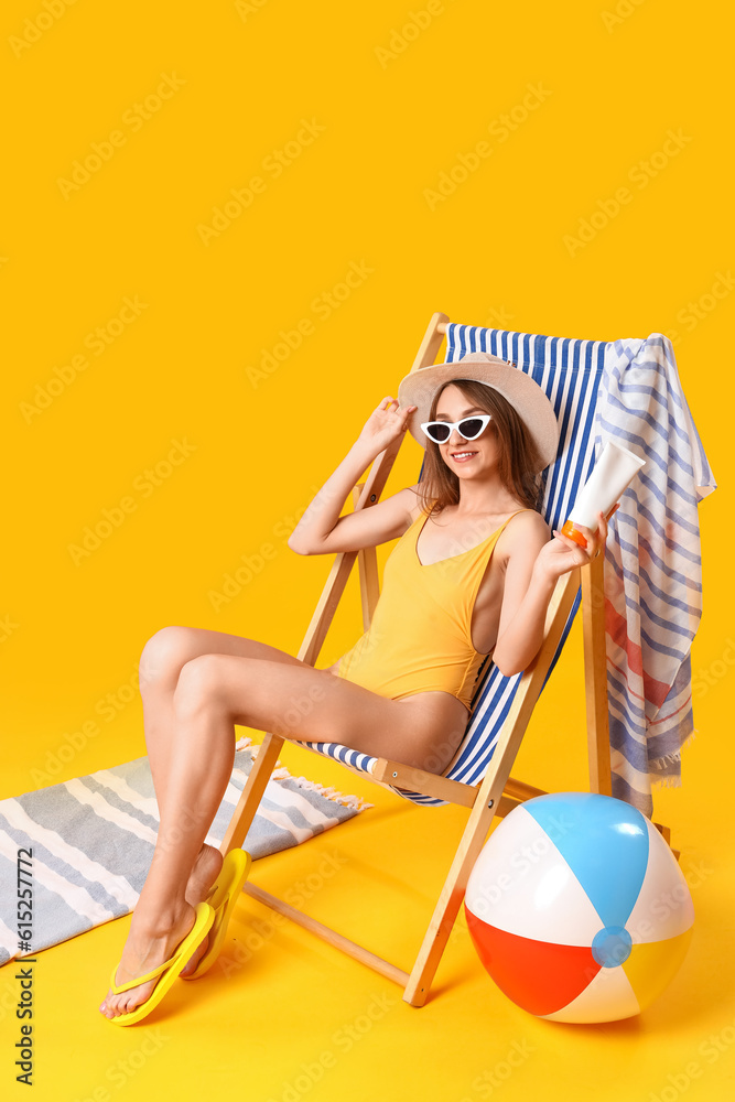 Young woman with sunscreen cream sitting in deck chair on yellow background