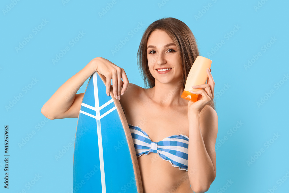 Young woman with sunscreen cream and surfboard on blue background