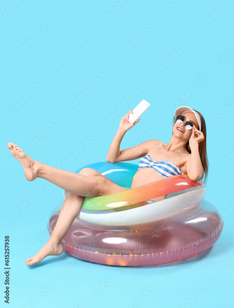 Young woman with sunscreen cream and inflatable rings on blue background