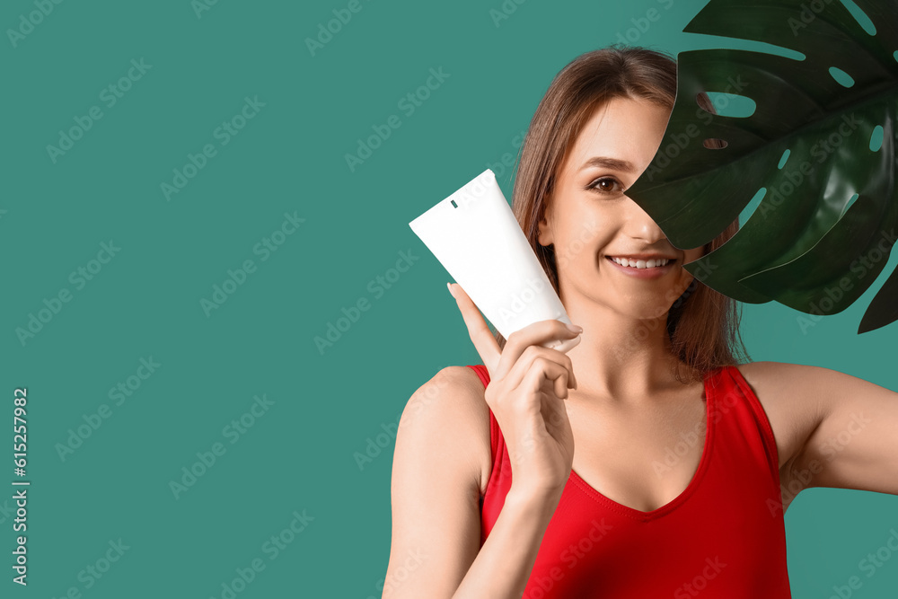 Young woman with sunscreen cream and palm leaf on green background