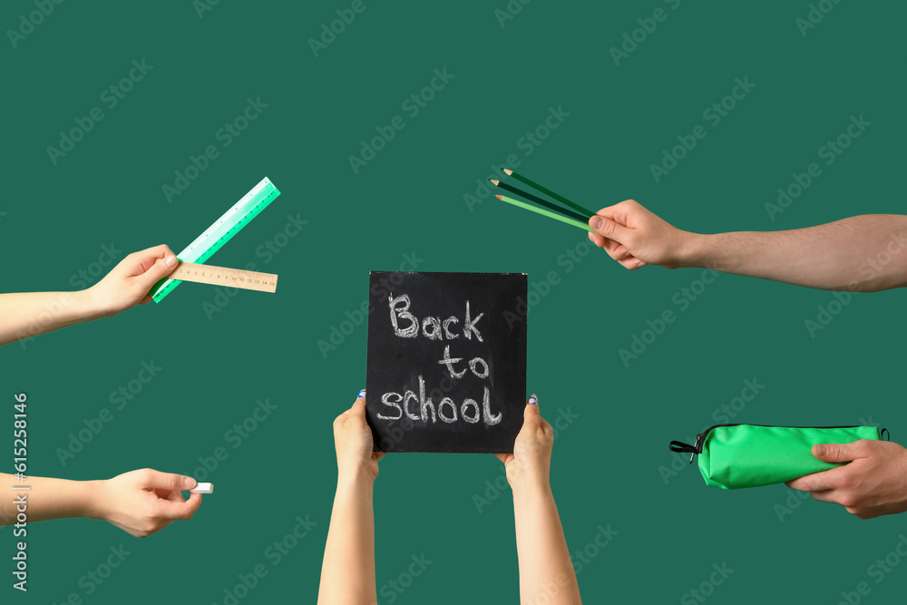 People holding chalkboard with text BACK TO SCHOOL and stationery on green background